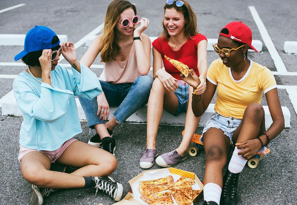 A diverse group of women sitting on the floor and eating pizza together