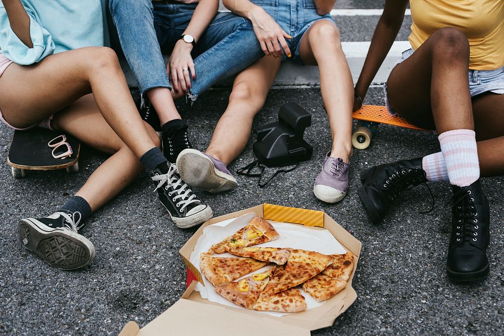 A diverse group of women sitting on floor eating pizza together
