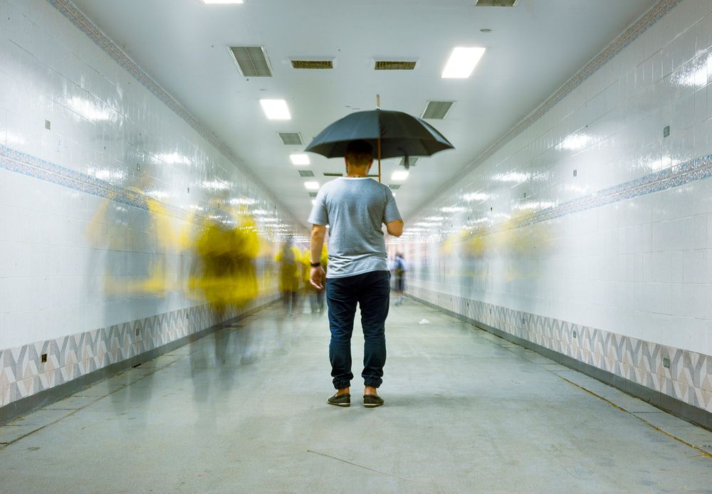 Rear view of a man holding umbrella with blurred people long exposure technique