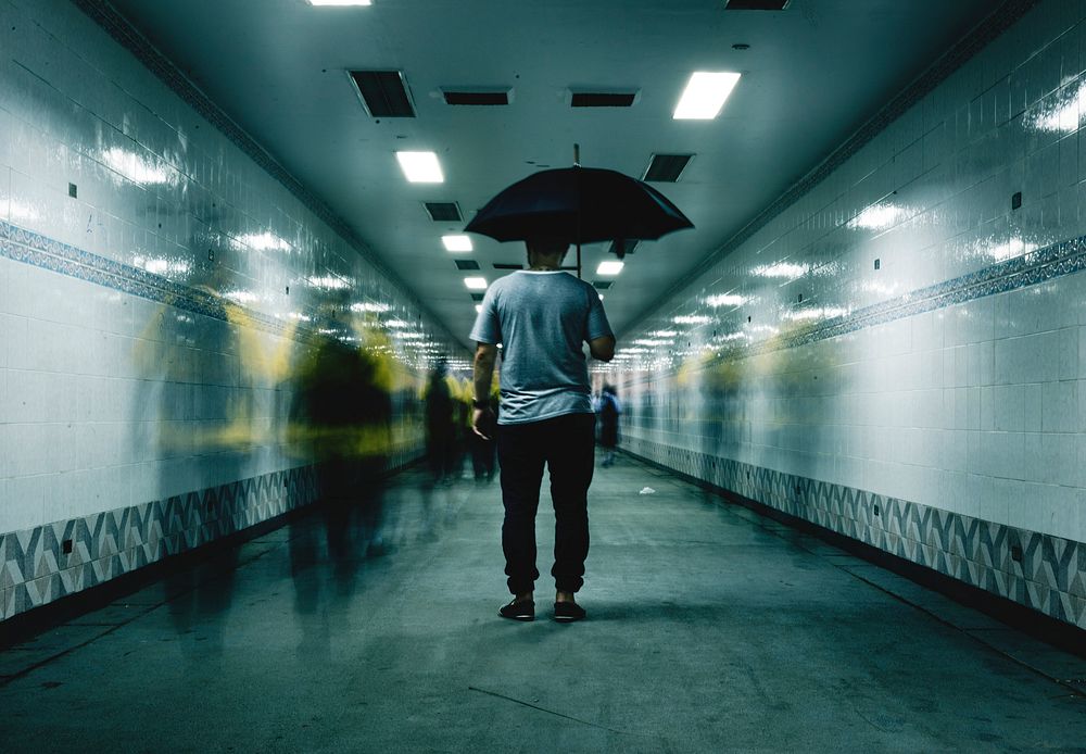 Rear view of a man holding umbrella with blurred people long exposure technique