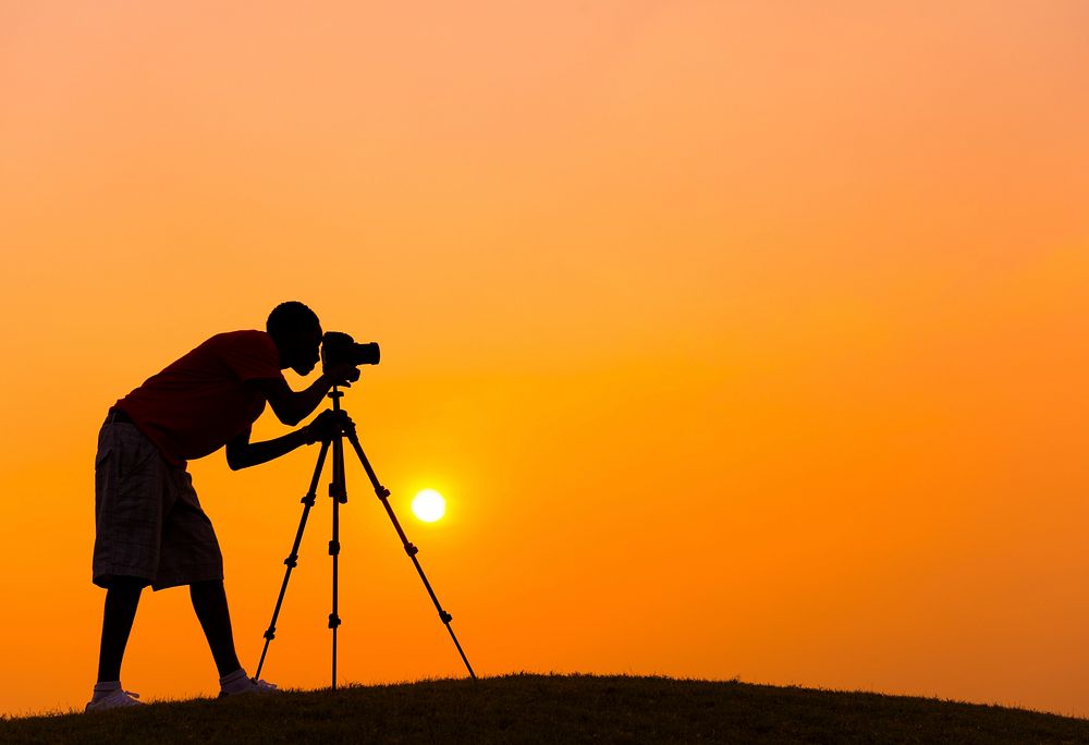 Camera man taking a photo outdoors with a sunset backdrop