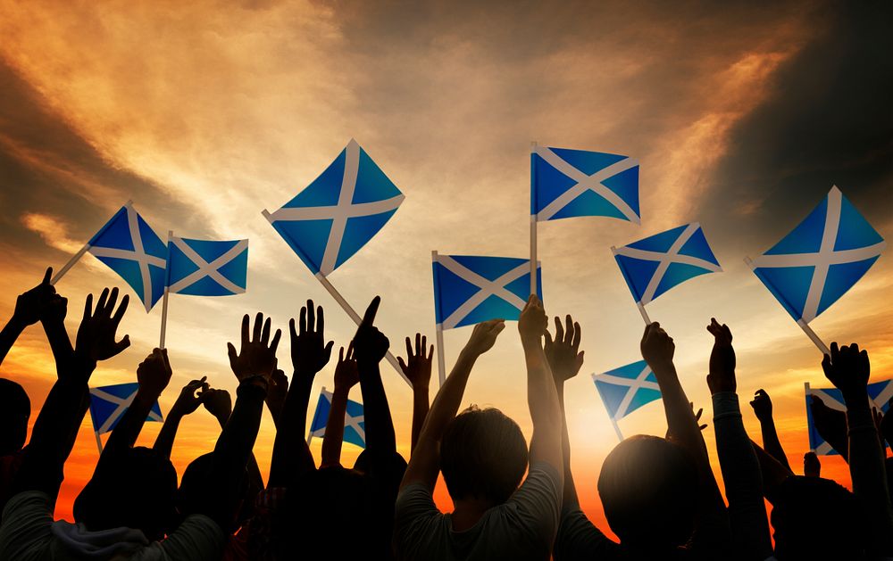 Group of People Waving Scottish Flags in Back Lit