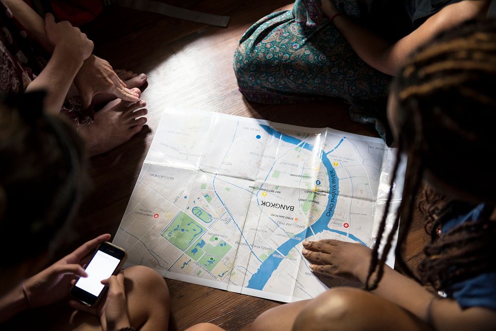A group of diverse tourists sitting on the wooden floor planning and using the map