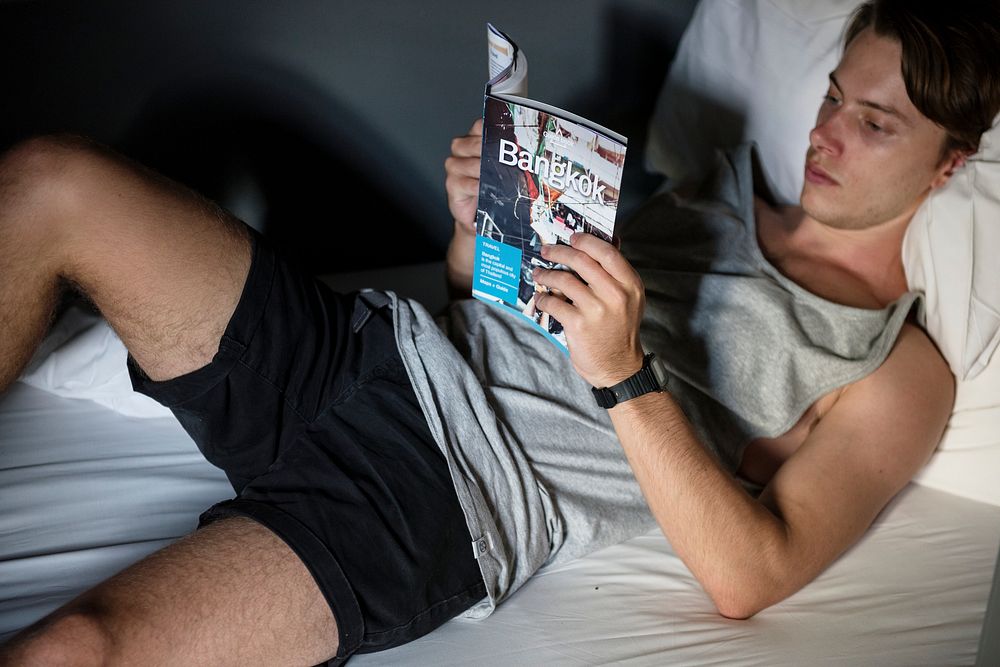 Caucasian man lying on the bed reading Bangkok Thailand travel guide book