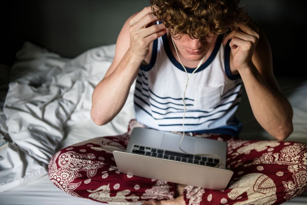 A Caucasian man sitting on the bed using a laptop