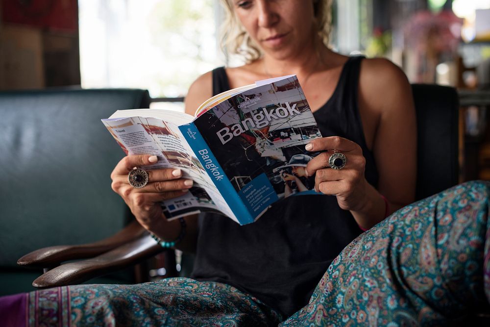 A Caucasian woman sitting and reading Bangkok Thailand travel guide book