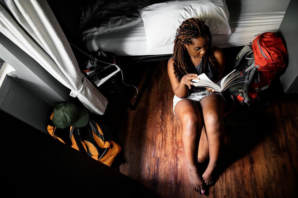 An African descent woman sitting on the wooden floor reading a book