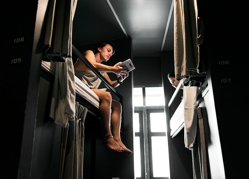 Caucasian man sitting on bunk bed reading Bangkok Thailand travel guide book