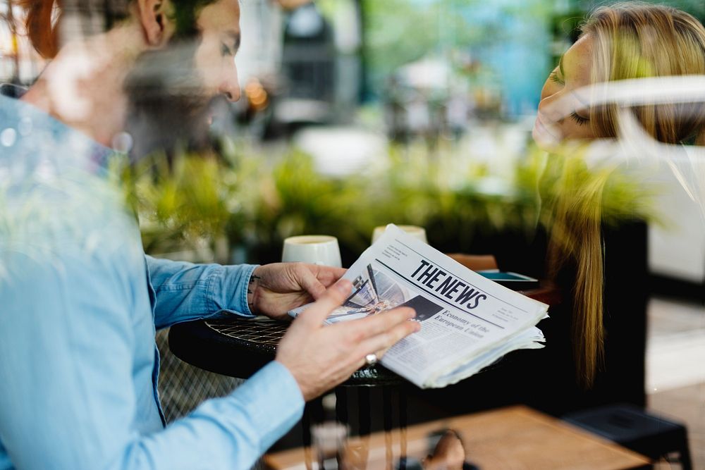 A man with beard showing newspaper to a woman