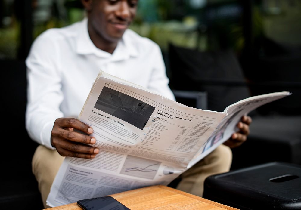 African descent man sitting reading a newspaper outdoor