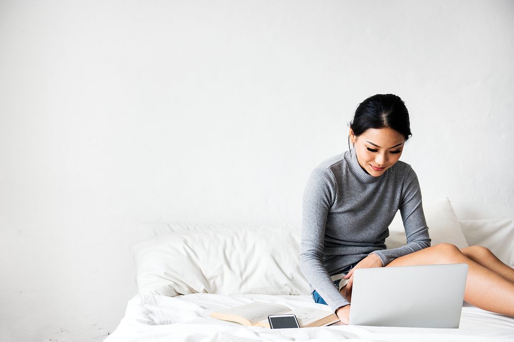 Asian woman using computer laptop on white bed