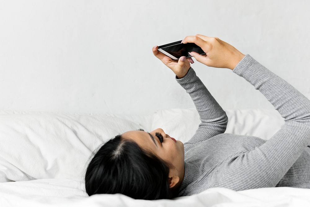 Asian woman lying on bed using mobile phone