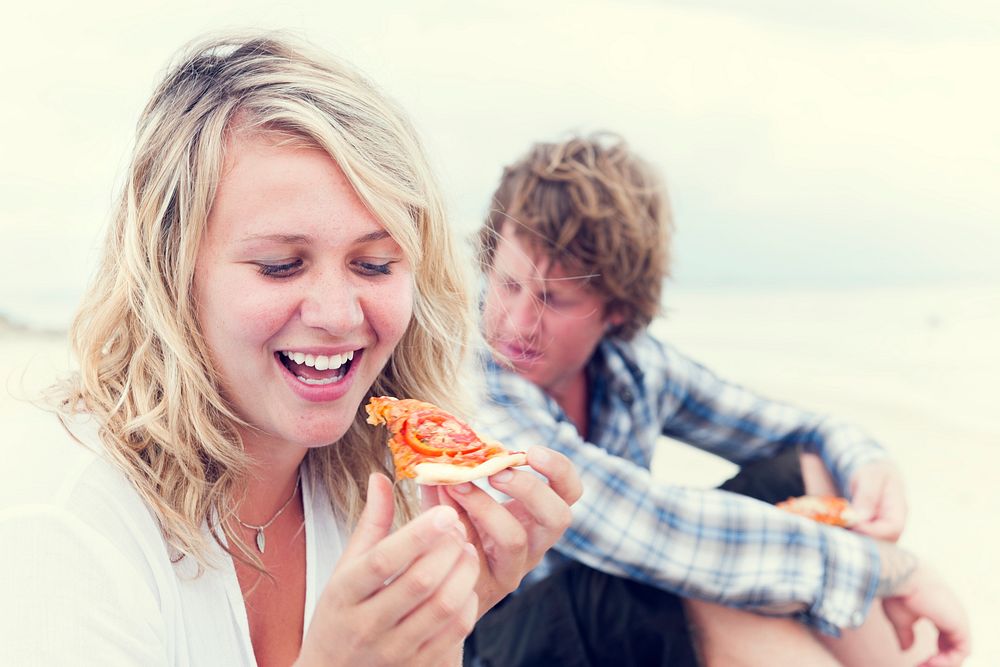 Blonde girl eating pizza on beach.