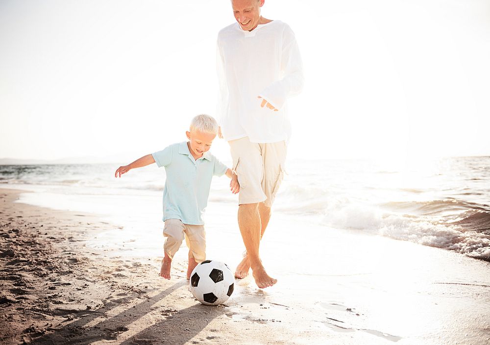 Dad and son playing soccer by the beach