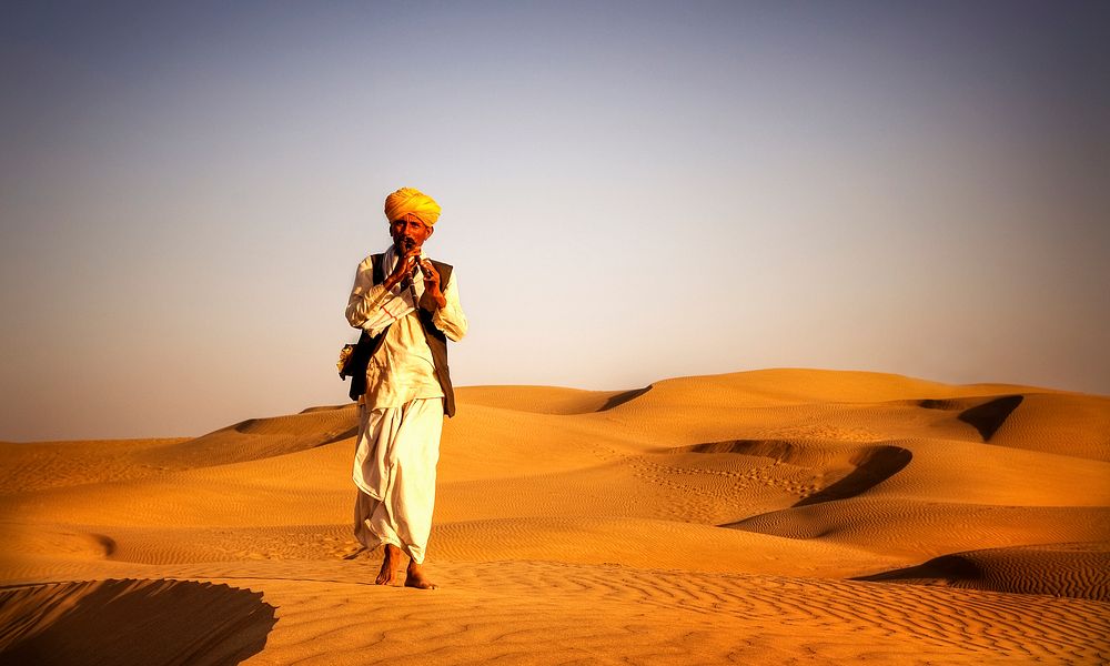 Indian man playing wind pipe in a desert.