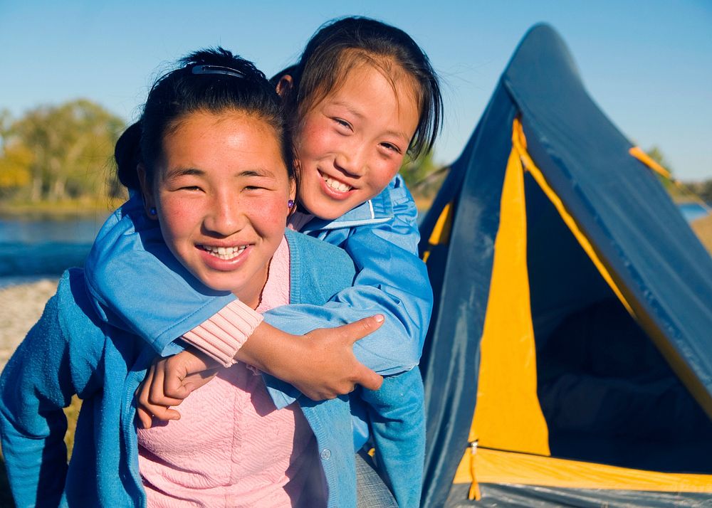 Happy Mongolian girls playing piggyback at campsite.