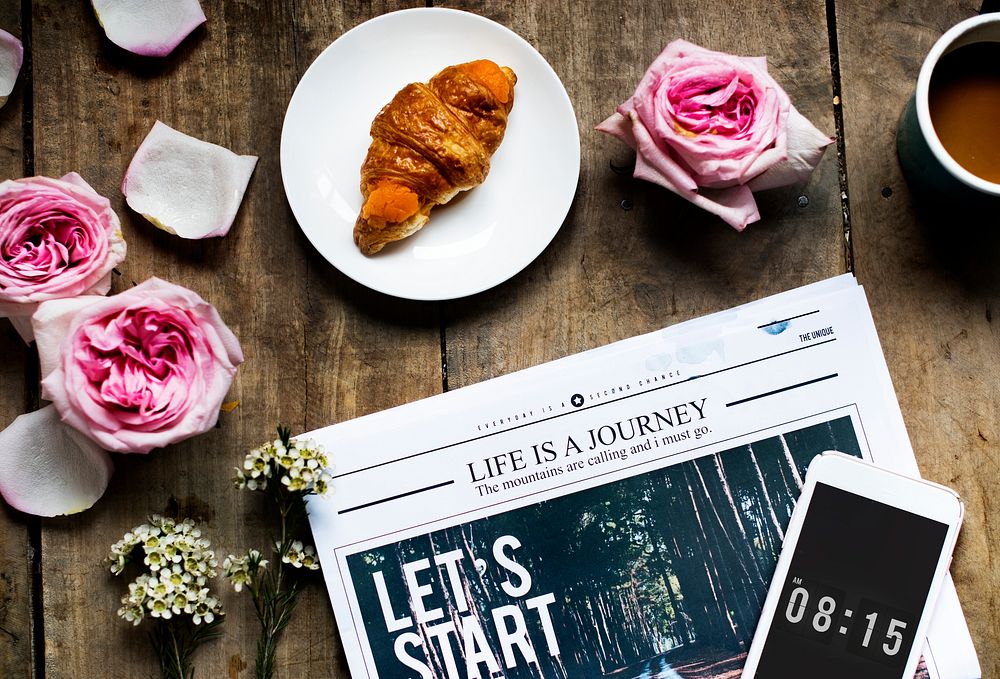 Aerial view of croissant and newspaper with roses decoration on wooden table