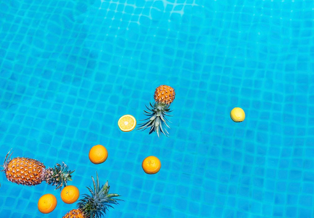 Aerial view of pineapple and oranges floating in swimming pool