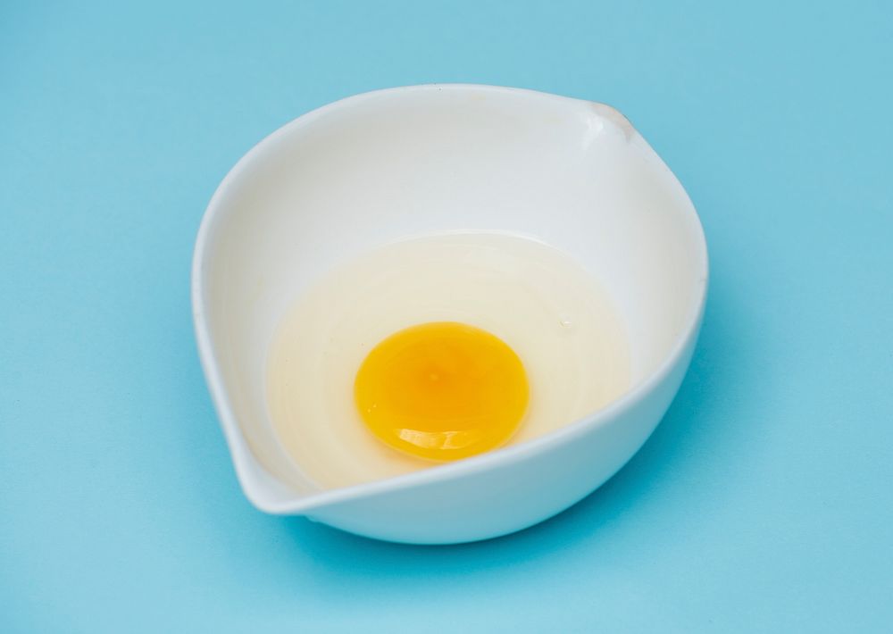 Single egg in the white bowl with blue background