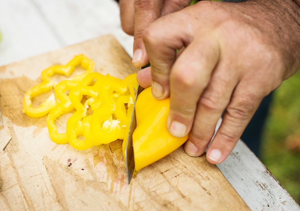 Hands holding a yellow bell pepper on a cutting board
