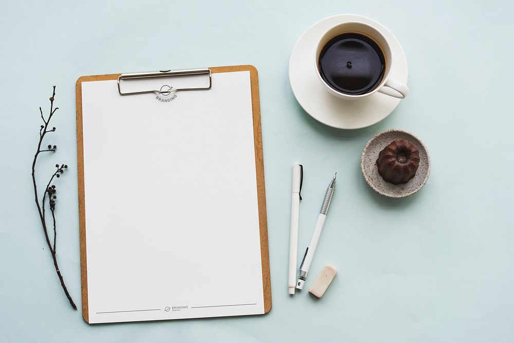 Aerial view of paper clipboard with coffee cup and cake