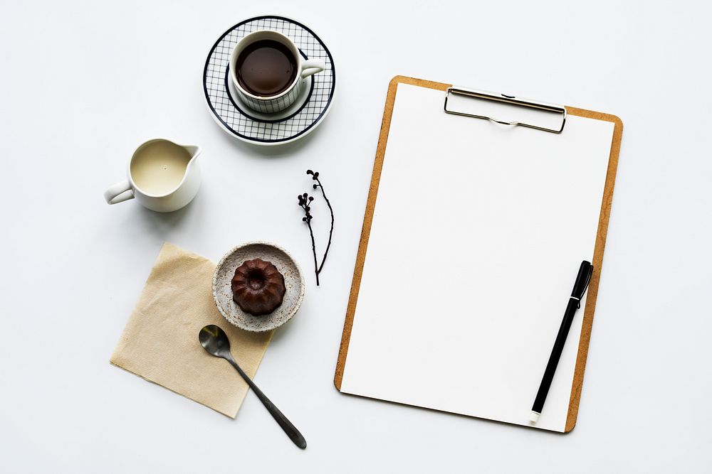 Aerial view of paper clipboard with coffee cup and cake
