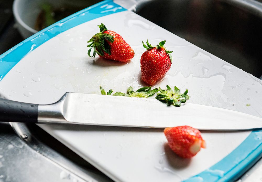Closeup of fresh strawberries on cutting board with knife at sink