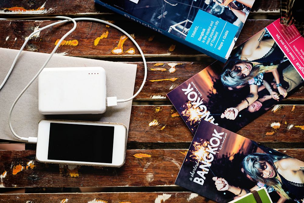 Mobile phone chargin with power bank lying with Bangkok Thailand travel guide book brochure