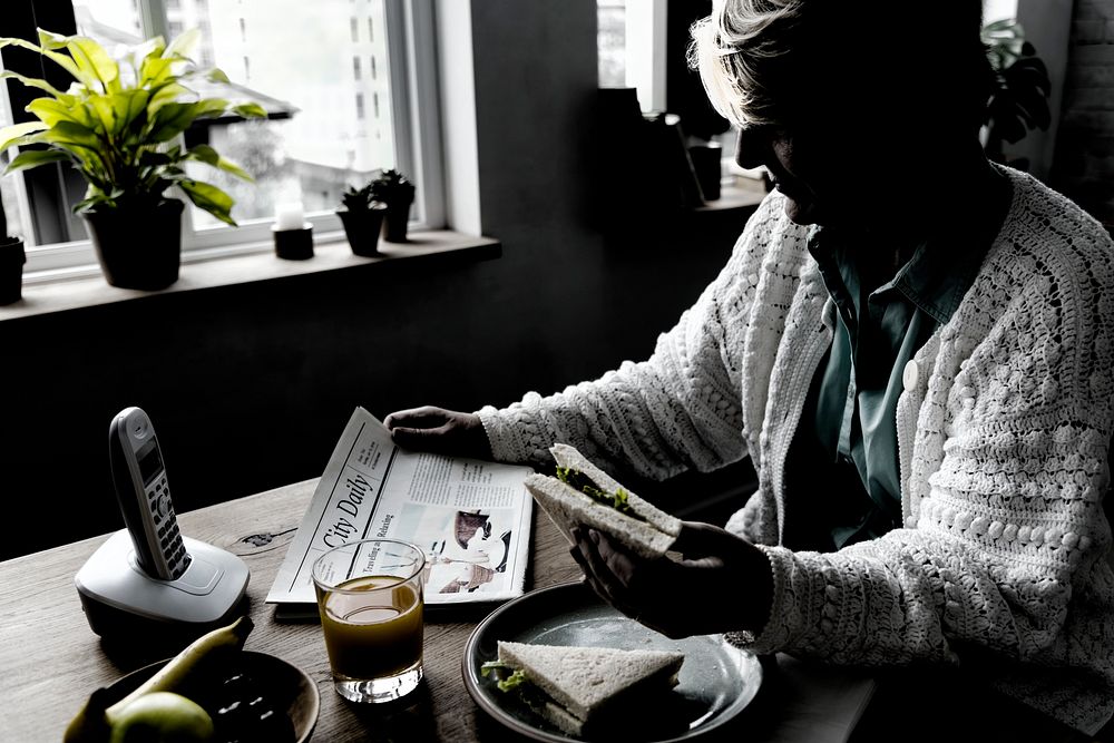 Senior Woman Eating Breakfast Reading Newspaper Concept