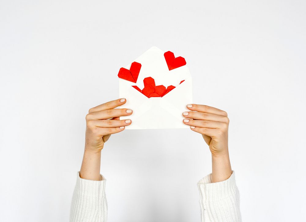 Hands holding envelope with hearts inside on white background