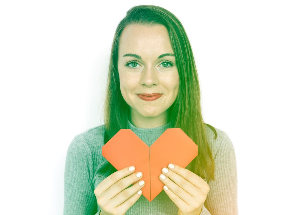 A caucasian woman is holding origami heart shape.
