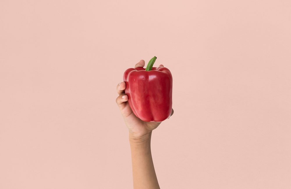 Hand holding a red bell pepper in a studio