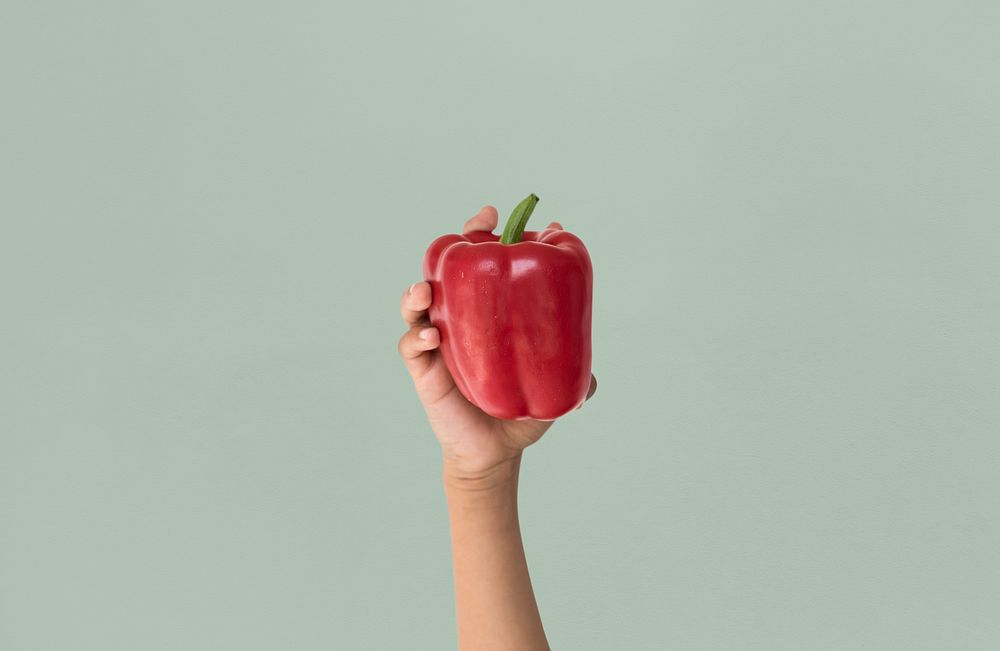 Hand holding a red bell pepper in a studio