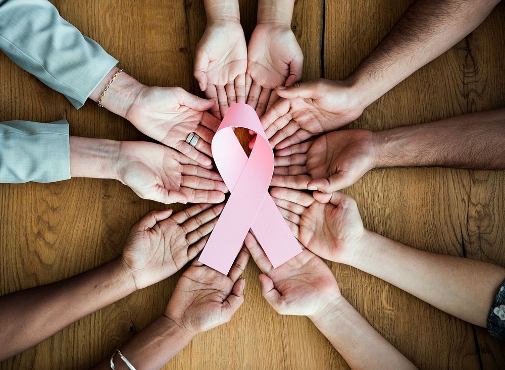 Group of diverse hands holding pink ribbon together representing breast cancer awareness and support