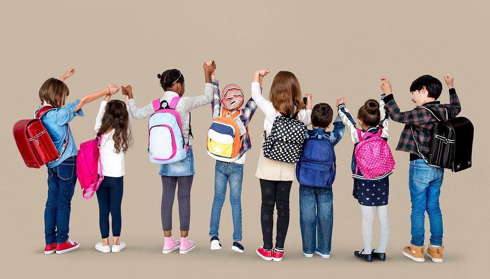 Rear view group of diverse kids standing in a row holdings hands in the air