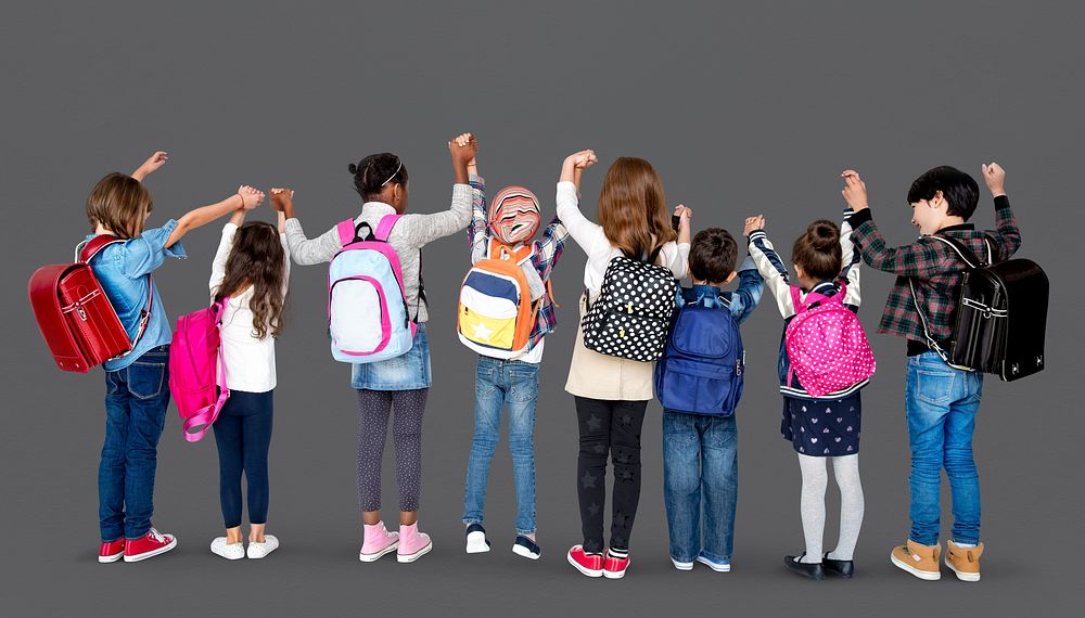 Rear view group of diverse kids standing in a row holdings hands in the air