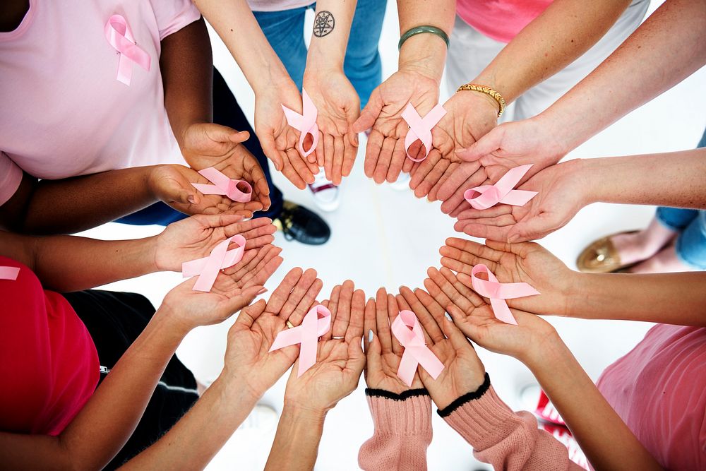 Group of hands holding pink ribbon for breast cancer awareness