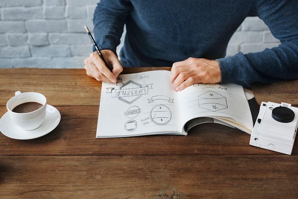 Closeup of hands drawing banners badges in drawing book on wooden table