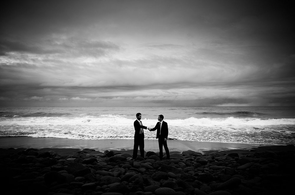 Two business guys shaking hands on the beach