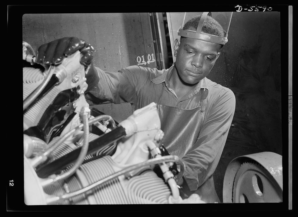 Production. Aircraft engines. A young African American worker stands ready to wash or "degrease" this airplane motor prior…