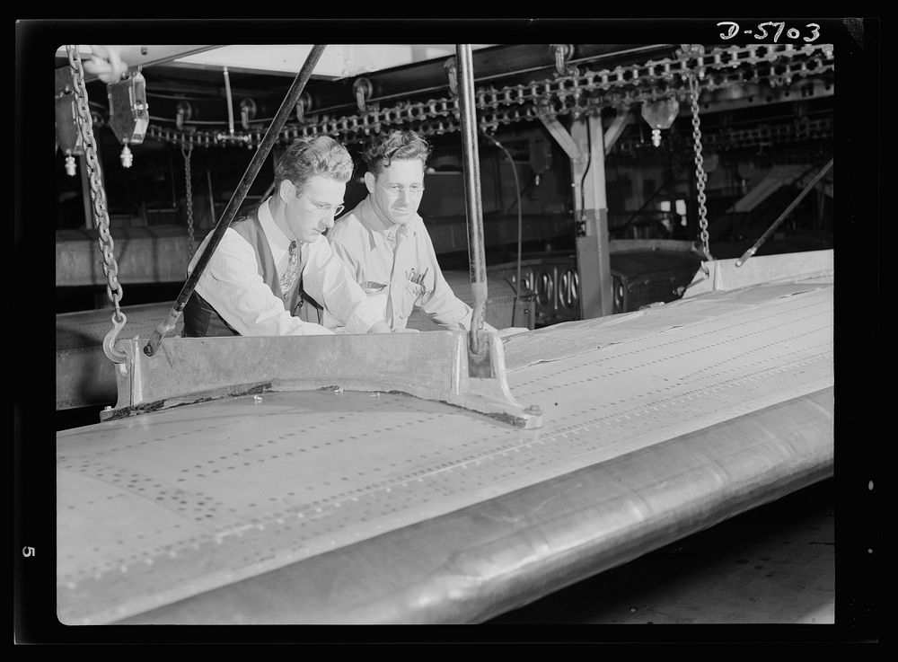 Production. Willow Run bomber plant. Checking almost-completed wing structure with blueprints, engineers at the great Willow…