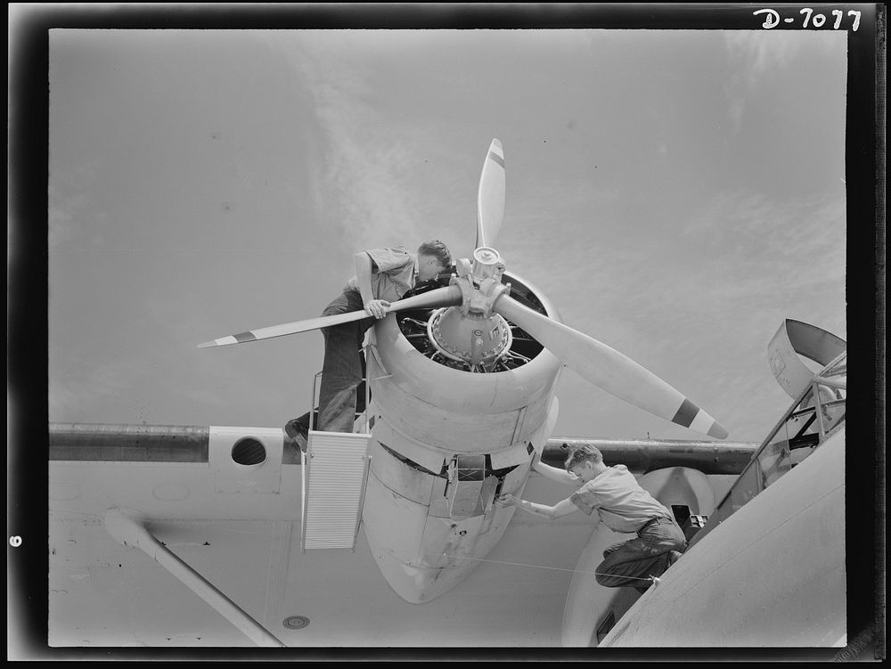 Naval air base, Corpus Christi, Texas. Perched at the nose of a Navy PBY flying ship, two sailors check the huge motor to…
