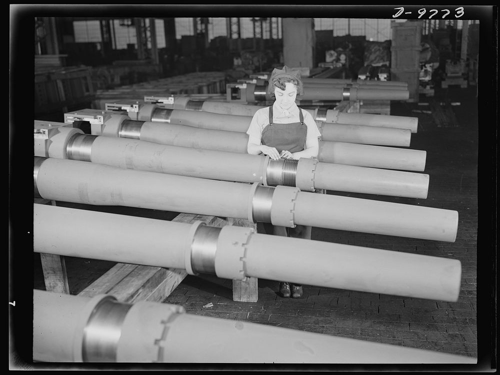Production. 105 mm. howitzers. Mrs. Mary Betchner inspecting one of the twenty-five cutters for burrs before inserting it in…