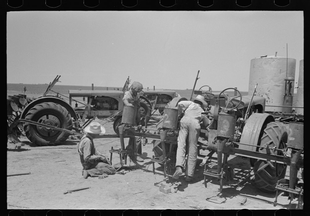 Day laborer changing plow points on tractor-drawn four-row planter. Gasoline tanks in the background, large farm near Ralls…