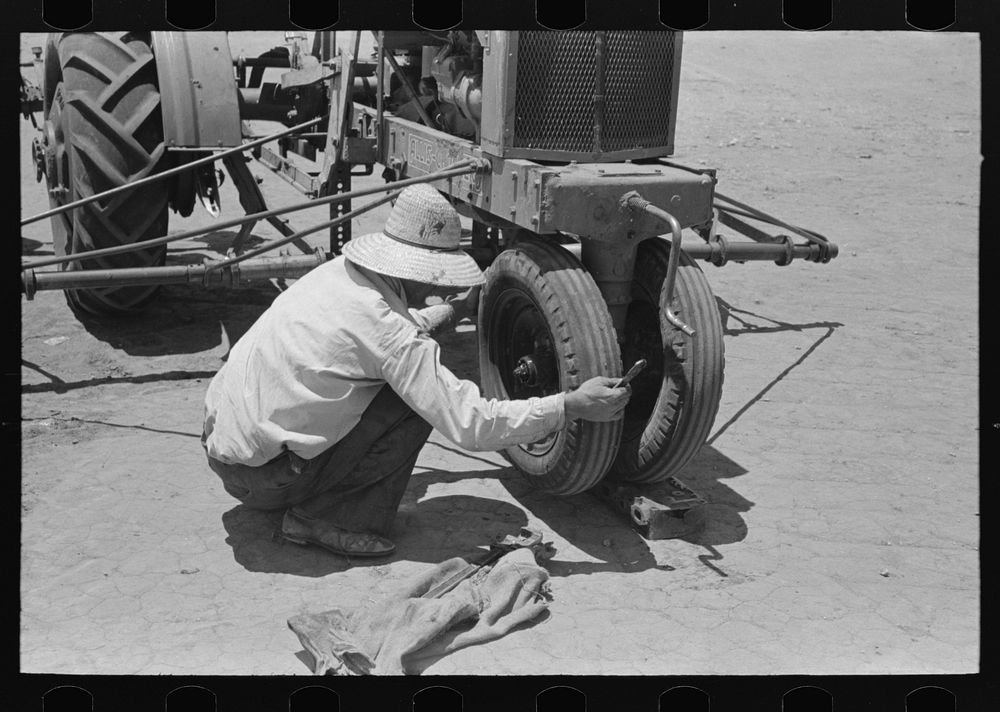 Day laborer testing play on front wheel bearing of tractor, farm near Ralls, Texas by Russell Lee