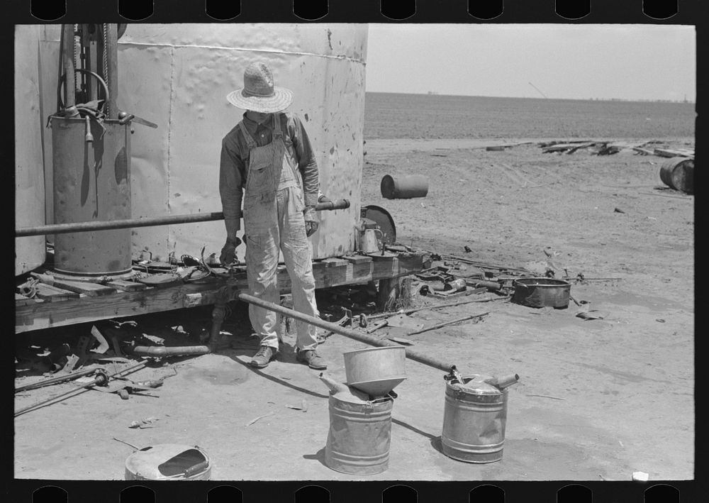 [Untitled photo, possibly related to: Day laborer filling five gallon cans with gasoline for use in tractors, large farm…