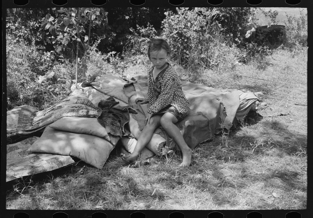 Child of agricultural day laborers camped near Spiro, Oklahoma. She is sitting on the bedroll. There was no bed in the camp.…