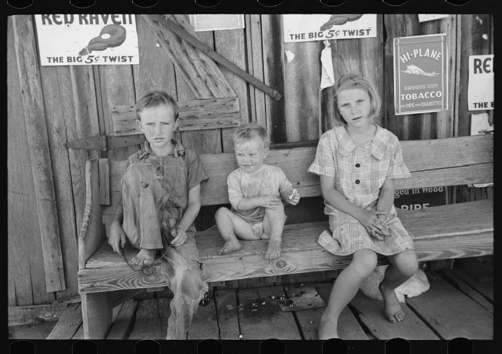 Children of agricultural day laborers sitting on bench in front of small store near Vian, Oklahoma by Russell Lee