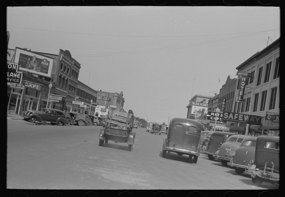 Main street of Muskogee, Oklahoma with migrants' car passing down the middle of it by Russell Lee