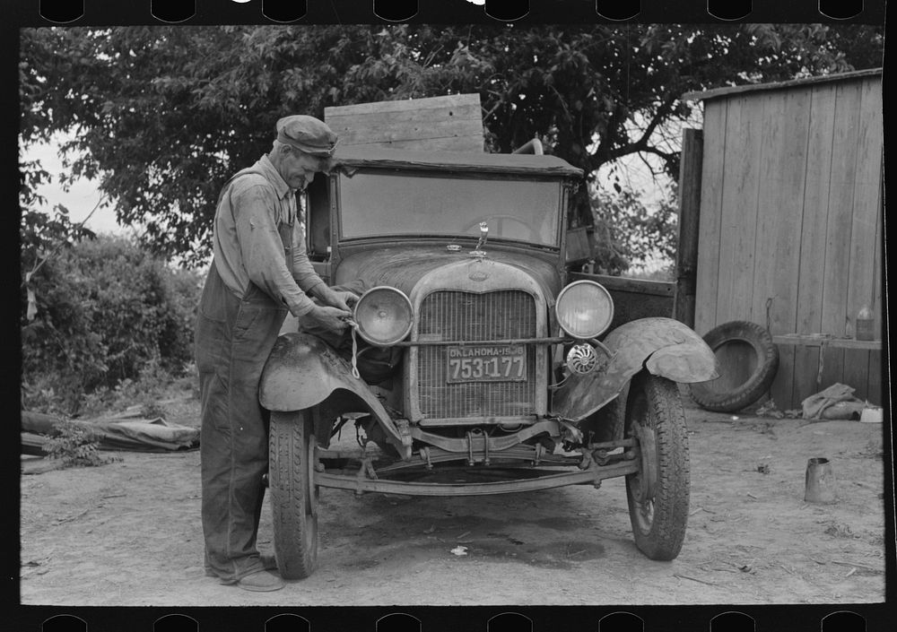 [Untitled photo, possibly related to: Elmer Thomas, migrant to California, tying sack of laundry onto front lamp bracket…